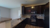 Located at 4515 Desantis Ct in Columbus, Ohio, this single-floor unit offers a well-designed layout with a cohesive, modern aesthetic throughout. The kitchen is a standout feature, showcasing rich dark espresso cabinetry that reaches toward the ceiling, granite-style countertops, a double stainless steel sink, and a tasteful stone tile backsplash. Black Whirlpool appliances — including an electric range, over-the-range microwave, and refrigerator — complete the functional and stylish cooking space. Wood-look flooring grounds the kitchen area, adding warmth and durability. The open living area flows naturally from the kitchen peninsula, offering a generous, carpet-floored space bathed in neutral tones. Soft gray walls and clean white trim give the living area a bright, modern feel, while a bold slate-gray accent wall adds visual depth and character near the bedroom entry. Track lighting provides targeted illumination in the transitional space. The bedroom connects seamlessly from the main living area and is finished with plush carpeting. The bathroom is clean and functional, featuring a soaking tub with an arched surround, built-in shelving, a shower rod, and crisp white fixtures throughout, all set against neutral gray walls.