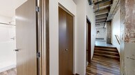 Located at 8 Tenth Street North in Moorhead, MN, this 2-bedroom, 2-bathroom loft-style residence offers a compelling blend of historic industrial character and modern finishes. The open living and kitchen area immediately showcases the space's most defining architectural features: exposed, weathered wood beam ceilings with visible plank decking overhead, original brick accent walls, and rustic structural columns that speak to the building's converted heritage. Rich, dark hardwood-style plank flooring runs throughout the main living area, grounding the space with warmth and continuity. The kitchen is equipped with dark espresso cabinetry, stainless steel appliances including a refrigerator and dishwasher, and a wall-mounted mini-split HVAC unit, ensuring year-round comfort. Natural light enters through multi-pane windows set into the exposed brick walls, adding brightness to the industrial aesthetic. Both bedrooms are finished with plush carpet and continue the exposed beam ceiling theme, with the primary bedroom offering a generous footprint. One bathroom features a full soaking tub with shower surround, while the second provides a walk-in shower stall with built-in corner shelving. A hallway and closet complete the well-organized layout of this distinctive and characterful urban residence.