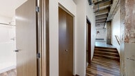 Located at 8 Tenth Street North in Moorhead, MN, this 2-bedroom, 2-bathroom loft-style residence offers a compelling blend of historic industrial character and modern finishes. The open living and kitchen area immediately showcases the space's most defining architectural features: exposed, weathered wood beam ceilings with visible plank decking overhead, original brick accent walls, and rustic structural columns that speak to the building's converted heritage. Rich, dark hardwood-style plank flooring runs throughout the main living area, grounding the space with warmth and continuity. The kitchen is equipped with dark espresso cabinetry, stainless steel appliances including a refrigerator and dishwasher, and a wall-mounted mini-split HVAC unit, ensuring year-round comfort. Natural light enters through multi-pane windows set into the exposed brick walls, adding brightness to the industrial aesthetic. Both bedrooms are finished with plush carpet and continue the exposed beam ceiling theme, with the primary bedroom offering a generous footprint. One bathroom features a full soaking tub with shower surround, while the second provides a walk-in shower stall with built-in corner shelving. A hallway and closet complete the well-organized layout of this distinctive and characterful urban residence.