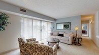 Located at 1200 Vineyard Dr in Broadview Heights, Ohio, this single-floor unit offers a well-organized and comfortable layout. The living room is a welcoming focal point, featuring soft carpet flooring, cool blue-gray accent walls, and a large sliding glass door dressed with vertical blinds that fill the space with natural light. A decorative framed mirror enhances the room's depth and brightness. Adjacent to the living area, the dining space provides an intimate setting with neutral walls accented by classic chair rail molding and carpet flooring, creating a calm atmosphere for everyday meals. The kitchen is efficiently designed with white cabinetry, white appliances including a refrigerator and stove, a built-in sink, and ample counter space, all set beneath warm yellow-toned walls. The bedroom is a serene retreat with plush carpet, soft blue-gray walls, and a generous closet with built-in shelving. A dedicated utility nook provides additional storage and folding space. The bathroom features marble-style tile flooring, a full tub-shower combination, a single vanity, and clean white finishes throughout. The overall ambiance of the unit is light, neutral, and move-in ready, with a cohesive design palette that flows seamlessly from room to room.
