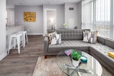 Located at 5143 Dundas St W in Toronto's Etobicoke neighbourhood, this single-floor unit offers a well-designed layout with a contemporary aesthetic throughout. The open-concept living area is bathed in natural light through expansive floor-to-ceiling windows dressed with vertical blinds, framing impressive views of the surrounding cityscape. Light wood-tone flooring runs through the main living spaces, complementing the neutral warm-grey palette on the walls.

The kitchen features white cabinetry, stainless steel appliances including a refrigerator, electric range, and built-in microwave, along with a generous island with a light quartz countertop and undermount sink — ideal for both cooking and casual dining. Track lighting overhead adds a clean, functional touch.

Multiple bedrooms offer comfortable retreats, each with large windows providing city or outdoor views, wood-tone flooring, and ample closet space. The unit includes two bathrooms finished with light tile flooring, white vanities, and clean, minimal fixtures — one with a shower-tub combination.

The entryway transitions smoothly between tiled and wood flooring, connecting the various spaces cohesively. A balcony accessible from the living area further enhances the sense of openness and connection to the surrounding urban environment.
