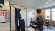 This dedicated fitness space at 4170 Green Clover Dr in Hilliard, Ohio, is thoughtfully designed to support a comprehensive workout routine. The room features a striking black-and-white checkered tile floor that gives the space a clean, gym-like aesthetic, complemented by neutral gray walls and a textured ceiling with recessed lighting.

The strength training area is anchored by a Hoist multi-station cable machine, offering a wide range of resistance exercises. A full dumbbell rack stocked with multiple weight increments provides additional free weight options for varied training needs. The cardio section is equally well-appointed, housing a SportsArt treadmill, an elliptical trainer, and a SportsArt upright stationary bike — all positioned to take advantage of natural light flowing in through multiple windows along one wall.

A wall-mounted flat-screen television is positioned for easy viewing from virtually any area of the room, making it easy to follow workout programs or simply stay entertained during exercise. A small console table offers a convenient surface for accessories and personal items. The space is accessed through a glass-panel door, connecting it seamlessly to the rest of the home. Overall, this fitness room delivers a fully functional, private gym experience in a well-organized and comfortable setting.