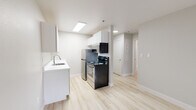Located at 5560 Library Lane in Colorado Springs, Colorado, this single-story unit presents a clean, modern interior defined by a neutral color palette and light wood-style flooring that runs consistently throughout the space. The overall design is minimal and functional, creating a bright, open atmosphere.

The kitchen is efficiently arranged with white shaker-style cabinetry extending to the ceiling, providing ample storage above and below. White countertops offer a clean workspace, complemented by a stainless steel single-basin sink with a modern faucet. Appliances include a stainless steel refrigerator, a black electric range with coil burners, and a stainless steel microwave. Recessed and flush-mount lighting keeps the kitchen well-illuminated.

The living area is open and generously proportioned, with smooth neutral walls and a window fitted with vertical blinds that allows natural light into the space. A baseboard heater runs along one wall, and the unobstructed floor plan provides flexibility for furniture arrangement.

The bathroom is well-appointed, featuring white subway tile surrounding a full soaking tub and shower, a white vanity with a single sink and mirror, and light wood-style flooring. A stacked washer and dryer unit is conveniently integrated into the bathroom, adding practical in-unit laundry access.
