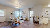 This single-floor residence is thoughtfully laid out to maximize functionality across its key living areas. The living room serves as the heart of the home, featuring wood-look flooring, a ceiling fan with light fixture, and multiple windows that invite natural light throughout the space. A built-in desk area with granite-style countertop provides a convenient workspace directly off the living room, while a hallway connects seamlessly to the private bedroom.

The bedroom is generously sized, offering a ceiling fan, wood-look flooring, a closet, and a window that brings in additional natural light. The kitchen is well-appointed with white cabinetry, granite-look countertops, a stainless steel sink, and matching appliances, all set against wood-look flooring. A dedicated dining area adjacent to the kitchen features open shelving and artwork, creating a refined yet functional setting.

Two full bathrooms are included, each outfitted with a tub-shower combination, white cabinetry for storage, and clean, neutral finishes. Throughout the entire residence, a consistent soft gray and white color palette, accented by warm gold tones, creates a cohesive and welcoming ambiance.