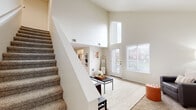 This two-story residence makes an immediate impression with its dramatic vaulted ceilings in the main living area, where towering walls and large windows flood the space with natural light. A carpeted staircase anchors the entry and leads to the upper level, while the open-concept lower floor connects the living room, dining area, and kitchen seamlessly. The living room offers generous space for multiple seating arrangements, complemented by a front entry door that adds additional light and outdoor access. Adjacent to the living area, the dining space features wood-look flooring and provides a natural transition into the kitchen. The kitchen is well-equipped with stainless steel appliances, including a refrigerator, dishwasher, and range, alongside light wood cabinetry and granite-style countertops. An in-unit washer and dryer is conveniently located off the main living area. The upper level hosts multiple bedrooms, each carpeted and thoughtfully laid out. One bedroom features a built-in desk, while another includes a walk-in closet. The primary bathroom is spacious, offering dual sinks with granite-style countertops, light wood cabinetry, hardwood flooring, and a separate glass-enclosed shower. Throughout, the warm neutral palette and consistent finishes create a cohesive and comfortable atmosphere.