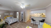 This single-floor studio unit in Houston, TX offers a thoughtfully arranged open-concept layout that seamlessly integrates the living, sleeping, and dining areas into one cohesive space. Light-toned hardwood-style flooring runs throughout, complemented by warm gray walls, white crown molding, and a textured ceiling that add a clean, classic character to the interior.

The main living area provides generous room for both a sleeping space and a separate sitting nook, which features a window dressed with vibrant curtains that allow natural light to filter in. A ceiling fan with a light fixture keeps the space comfortable year-round. A breakfast bar with bar seating connects the living area to the kitchen, making it ideal for casual dining.

The galley-style kitchen is efficiently designed with white cabinetry, granite-look countertops, and white appliances including a stove and full-size refrigerator. Upper and lower cabinets offer ample storage throughout.

A walk-in closet provides excellent storage, while the bathroom is finished with clean white tile and includes a full bathtub and shower combination. The overall ambiance is bright, practical, and welcoming, making this a well-appointed unit suited for comfortable everyday living in the heart of Houston.