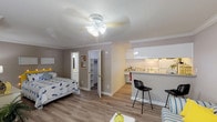 This single-floor studio unit in Houston, TX offers a thoughtfully arranged open-concept layout that seamlessly integrates the living, sleeping, and dining areas into one cohesive space. Light-toned hardwood-style flooring runs throughout, complemented by warm gray walls, white crown molding, and a textured ceiling that add a clean, classic character to the interior.

The main living area provides generous room for both a sleeping space and a separate sitting nook, which features a window dressed with vibrant curtains that allow natural light to filter in. A ceiling fan with a light fixture keeps the space comfortable year-round. A breakfast bar with bar seating connects the living area to the kitchen, making it ideal for casual dining.

The galley-style kitchen is efficiently designed with white cabinetry, granite-look countertops, and white appliances including a stove and full-size refrigerator. Upper and lower cabinets offer ample storage throughout.

A walk-in closet provides excellent storage, while the bathroom is finished with clean white tile and includes a full bathtub and shower combination. The overall ambiance is bright, practical, and welcoming, making this a well-appointed unit suited for comfortable everyday living in the heart of Houston.