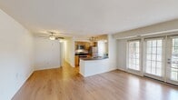 This 890-square-foot, single-floor residence at 8800 Queensmere Place in Richmond, Virginia offers 2 bedrooms and 2 bathrooms in a clean, functional layout. Light hardwood flooring runs throughout the unit, lending a bright and cohesive feel to every room. The open-concept kitchen and living area serves as the heart of the home, featuring warm honey-toned cabinetry, dark countertops, a peninsula with a sink, stainless steel appliances including a refrigerator and dishwasher, and track lighting overhead. Natural light filters in through multiple windows and a set of glass French doors in the living area. The kitchen includes ample upper and lower cabinet storage and a window overlooking greenery outside. Both bedrooms feature the same hardwood flooring and neutral white walls, with the primary bedroom spanning 160 square feet and providing access to a dedicated closet. The two bathrooms include a full bath with a tub-shower combination and chrome fixtures, and a second bath with a pedestal sink and toilet. A dedicated laundry room houses a full-size washer and dryer alongside an in-unit water heater, adding everyday convenience. The unit's clean, neutral palette and practical floor plan make it a versatile and functional living space.
