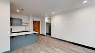 Located at 1216 North Superior Street, Unit 306 in Spokane, WA, this thoughtfully designed single-floor unit blends modern aesthetics with functional living. The open-concept layout connects the kitchen and living area seamlessly, creating a bright and airy atmosphere enhanced by recessed lighting and light wood-tone luxury vinyl plank flooring throughout.

The kitchen is a standout feature, showcasing gray shaker-style cabinetry, a white quartz countertop island with bar seating, and a full suite of stainless steel appliances including a refrigerator, electric range, and microwave. Open shelving adds a contemporary touch, while ample cabinet storage ensures practicality. A single-basin sink completes the space.

The living area is generously proportioned and flows naturally from the kitchen, offering flexibility for various furniture arrangements. A warm, solid wood door adds a distinctive architectural character, complementing the otherwise clean, modern palette of crisp white walls and dark baseboards.

The bedroom is bathed in natural light through a tall, classically trimmed window that frames outdoor greenery, lending a serene quality to the room. A baseboard heater ensures year-round comfort.

The bathroom is appointed with a vessel sink atop a quartz vanity, gray cabinetry with brushed nickel hardware, a mirrored medicine cabinet, and a tiled shower area, all combining to deliver a refined and polished finish.
