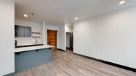Located at 1216 North Superior Street, Unit 306 in Spokane, WA, this thoughtfully designed single-floor unit blends modern aesthetics with functional living. The open-concept layout connects the kitchen and living area seamlessly, creating a bright and airy atmosphere enhanced by recessed lighting and light wood-tone luxury vinyl plank flooring throughout.

The kitchen is a standout feature, showcasing gray shaker-style cabinetry, a white quartz countertop island with bar seating, and a full suite of stainless steel appliances including a refrigerator, electric range, and microwave. Open shelving adds a contemporary touch, while ample cabinet storage ensures practicality. A single-basin sink completes the space.

The living area is generously proportioned and flows naturally from the kitchen, offering flexibility for various furniture arrangements. A warm, solid wood door adds a distinctive architectural character, complementing the otherwise clean, modern palette of crisp white walls and dark baseboards.

The bedroom is bathed in natural light through a tall, classically trimmed window that frames outdoor greenery, lending a serene quality to the room. A baseboard heater ensures year-round comfort.

The bathroom is appointed with a vessel sink atop a quartz vanity, gray cabinetry with brushed nickel hardware, a mirrored medicine cabinet, and a tiled shower area, all combining to deliver a refined and polished finish.