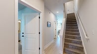 This thoughtfully designed three-story residence offers five bedrooms, six bathrooms, and generous living space distributed evenly across all three floors. The open-concept kitchen and living area anchor the home with a bright, modern aesthetic. The kitchen features gray cabinetry, stainless steel appliances including a full-size refrigerator and microwave, a central island with bar seating, track lighting overhead, and light hardwood flooring — creating an efficient and stylish space ideal for everyday living and entertaining. The adjacent living room is bathed in natural light from large windows with views of lush greenery, complemented by a ceiling fan and light hardwood floors. Each of the five bedrooms is carpeted and well-lit with natural light streaming through large windows dressed with sheer curtains and blinds, with ceiling fans providing added comfort. Bedrooms are accompanied by dedicated closets featuring wire shelving systems for organized storage. The six bathrooms maintain a clean, neutral palette with hardwood-style flooring, including bathrooms with full tub-shower combinations and powder rooms with pedestal sinks. Hallways are finished with light hardwood flooring and white panel doors with black hardware, while carpeted staircases with white railings connect all three floors seamlessly.