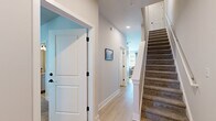 This thoughtfully designed three-story residence offers five bedrooms, six bathrooms, and generous living space distributed evenly across all three floors. The open-concept kitchen and living area anchor the home with a bright, modern aesthetic. The kitchen features gray cabinetry, stainless steel appliances including a full-size refrigerator and microwave, a central island with bar seating, track lighting overhead, and light hardwood flooring — creating an efficient and stylish space ideal for everyday living and entertaining. The adjacent living room is bathed in natural light from large windows with views of lush greenery, complemented by a ceiling fan and light hardwood floors. Each of the five bedrooms is carpeted and well-lit with natural light streaming through large windows dressed with sheer curtains and blinds, with ceiling fans providing added comfort. Bedrooms are accompanied by dedicated closets featuring wire shelving systems for organized storage. The six bathrooms maintain a clean, neutral palette with hardwood-style flooring, including bathrooms with full tub-shower combinations and powder rooms with pedestal sinks. Hallways are finished with light hardwood flooring and white panel doors with black hardware, while carpeted staircases with white railings connect all three floors seamlessly.