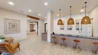 Located at 5026 Zion Rd in Garland, TX, this thoughtfully designed single-floor space offers a generous, open layout that blends modern coastal aesthetics with warm, inviting details. The entry area features a prominent bar counter with fluted paneling, warm rattan pendant lights, and patterned encaustic tile flooring that sets an elegant tone. Exposed white brick columns and a shiplap ceiling add architectural character while maintaining a bright, airy atmosphere. A central lounge area boasts floor-to-ceiling black-framed windows that flood the space with natural light and offer views of the surrounding outdoors. Exposed wood beams and a statement circular chandelier lend warmth and visual interest overhead. The dining area is anchored by a long communal table beneath a sleek pendant light, complemented by patterned wallpaper, white board-and-batten wainscoting, and light wood flooring. A smaller, intimate dining nook with a round marble-top table provides a more private setting. The conference room features a tiered fabric chandelier, built-in shelving, a wall-mounted display, and subtle plaid wallpaper, creating a refined yet functional meeting environment. A cozy seating lounge with neutral upholstered furnishings rounds out the space, offering a relaxed retreat within this well-appointed facility.