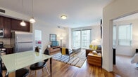 Located at 121 Towne St in Stamford, Connecticut, this well-appointed single-floor residence offers a thoughtfully designed layout with modern finishes throughout. The open-concept living and dining area is anchored by rich hardwood flooring, large floor-to-ceiling windows that invite abundant natural light, and access to a private balcony. The living space features a comfortable seating area accented with bold yellow and grey tones, complemented by a curated gallery wall arrangement. The kitchen is outfitted with dark espresso cabinetry, granite countertops, and a full suite of stainless steel appliances, including a gas range, microwave, and refrigerator, flowing seamlessly into the dining area. The residence includes two bedrooms, each carpeted for comfort. The primary bedroom boasts large windows with exterior views, generous closet space, and a warm, restful ambiance. The second bedroom is equally well-proportioned with ample natural light. Two full bathrooms feature dark wood vanities with white countertops, large mirrors, and a combination tub and shower with glass sliding doors, finished with clean tile flooring throughout. This residence offers a refined and functional living experience in the heart of Stamford.
