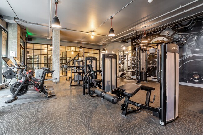 Gimnasio comunitario con máquinas de pesas, bicicletas cardiovasculares y espejos - Pike Motorworks