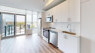 This well-appointed 2-bedroom, 2-bathroom unit is designed with a clean, contemporary aesthetic that maximizes both function and style. Light wood-tone flooring flows consistently throughout the space, complemented by crisp white walls and bright flush-mount lighting that create an airy, cohesive feel.

The kitchen is a standout feature, equipped with stainless steel appliances including a range, microwave, dishwasher, and refrigerator. White cabinetry extends to the ceiling for generous storage, while a neutral quartz countertop and subway tile backsplash add a polished finish. Floor-to-ceiling windows and a sliding glass door lead to a private balcony, flooding the kitchen with natural light and providing open urban views.

The primary bedroom benefits from an expansive floor-to-ceiling window that frames sweeping city rooftop views, offering an abundance of natural light. Each bedroom includes closet space for ample storage. The second bedroom features a sleek glass-panel sliding closet door.

Both bathrooms are finished in a minimalist style with white tile and chrome fixtures. One bathroom offers a glass-enclosed walk-in shower, while the second features a full soaker tub with shower, both accented by marble-look tile flooring. Two hallways connect the rooms efficiently, completing this thoughtfully designed urban residence.