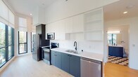 Located at 1901 Blake Ave in the desirable Silver Lake neighborhood of Los Angeles, this contemporary two-story space showcases a clean, modern aesthetic with thoughtfully selected finishes throughout. Light wood flooring flows consistently across both levels, complementing the crisp white walls and recessed lighting that together create a bright, open ambiance.

The entry level welcomes visitors through a dark-framed glass door, leading to a staircase with a sleek black metal handrail and natural wood treads. The kitchen is well-appointed with two-tone cabinetry—matte charcoal lower cabinets paired with white upper cabinets that extend to the ceiling—along with white countertops, a matte black faucet, and stainless steel appliances including a refrigerator, range, microwave, and dishwasher.

The bathrooms feature striking geometric cube-patterned tile flooring in neutral tones, complemented by matte black fixtures. One bathroom includes a walk-in shower with frameless glass panels, while another offers a navy blue vanity cabinet topped with a white countertop.

The upper level opens to a generously proportioned living area lined with large black-framed windows that frame lush tree canopy views, flooding the space with natural light. A frosted glass panel near the staircase adds a refined architectural detail, enhancing both privacy and design continuity throughout.