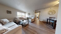This single-floor residence offers a thoughtfully designed layout that balances comfort and functionality. The open-concept living area is anchored by warm hardwood-style flooring, a textured ceiling, and large windows that invite an abundance of natural light. The living room accommodates generous seating and a central coffee table, while decorative wall accents lend a welcoming, curated feel. Adjacent to the living area, a dedicated dining space features room for a full dining table and chairs, accented by wall art that complements the neutral color palette throughout.

The galley-style kitchen is efficiently arranged with grey cabinetry, light granite-look countertops, and black appliances including a range and refrigerator. Open shelving and ample cabinet storage make the kitchen both practical and visually appealing.

The bedroom is a calm, spacious retreat finished with plush carpet, a large window for natural light, and room for a full bedroom suite. A hallway connects the main living areas to the private spaces, including a bathroom that features a full tub-shower combination. Notably, in-unit laundry with a washer and dryer is conveniently located within the residence, adding a practical and sought-after amenity to this comfortable, move-in-ready space.