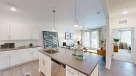 Located at 23 Evolve Parkway in Palm Coast, Florida, this thoughtfully designed one-bedroom, one-bathroom residence offers a well-organized single-floor layout with a bright, modern aesthetic throughout. The open-concept living area seamlessly combines the kitchen, dining, and living spaces into one cohesive hub. The kitchen is a standout feature, showcasing white shaker-style cabinetry extending to the ceiling, dark quartz countertops, a subway tile backsplash, stainless steel appliances including a range, microwave, refrigerator, and dishwasher, and a large island with seating for three — all illuminated by stylish pendant lighting. The living area is bathed in natural light and anchored by French doors that open to an outdoor view, with a ceiling fan adding comfort. Light wood-style flooring runs throughout the main living spaces, while plush carpet adds warmth to the bedroom. The bedroom is comfortably sized with a ceiling fan, a window with natural light, and direct access to closet space. The bathroom features white cabinetry, quartz countertops, and wood-style flooring. Additional conveniences include an in-unit laundry room and a pantry, rounding out this efficient and well-appointed residence.