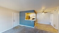 This single-story residence offers a functional and practical layout designed to maximize comfort and usability. The open living area is finished with wall-to-wall carpet and features a ceiling fan overhead. A distinctive blue accent wall frames the kitchen pass-through, which opens into a galley-style kitchen equipped with white cabinetry, light countertops, a stainless steel refrigerator, an electric range, and a utility sink. The kitchen also benefits from recessed lighting and wood-style flooring that extends throughout the cooking and dining areas. A door within the kitchen provides access to an in-unit laundry area. The living room is anchored by a sliding glass door fitted with vertical blinds, allowing natural light to filter in while providing outdoor access. The two bedrooms are carpeted and each feature windows with blinds that bring in additional natural light. The primary bedroom connects to a vanity area with a large mirror and a walk-in closet. The full bathroom is finished with wood-style flooring and includes a single-sink vanity with white cabinetry, a toilet, and a tub-shower combination. Clean, neutral tones throughout the space contribute to a bright and cohesive overall ambiance.