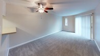 This single-story unit offers a practical and comfortable layout across two bedrooms and one full bathroom. The living room serves as the central gathering space, featuring neutral-toned carpet, a ceiling fan with light fixture, and a pass-through opening that connects to the kitchen, promoting an open feel. A sliding glass door fitted with vertical blinds provides natural light and direct outdoor access. The galley-style kitchen is efficiently designed with white shaker cabinetry, light countertops, wood-look flooring, a stainless steel sink, and black appliances including a refrigerator, electric range, microwave, and dishwasher. Both bedrooms are carpeted and finished with neutral walls and white baseboards. One bedroom features a sliding glass door with vertical blinds, while the other includes a narrow window for additional natural light. The full bathroom is outfitted with a white vanity, light countertop, a large mirror with overhead lighting, and a tub-shower combination with tiled surround and chrome fixtures. Throughout the unit, clean lines, consistent neutral tones, and practical finishes create a cohesive and functional living environment.