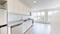 Located at 87 Union St in New Haven, Connecticut, this efficiently designed single-floor unit offers a clean, contemporary aesthetic throughout. The open-concept layout seamlessly connects the kitchen to the living area, maximizing the sense of space and promoting an airy, functional flow.

The kitchen is thoughtfully outfitted with crisp white shaker cabinetry extending to the ceiling for ample storage, gray quartz-style countertops, and a full suite of stainless steel appliances including an electric range, over-the-range microwave, dishwasher, and refrigerator. Light wood-tone flooring runs continuously throughout, adding warmth to the modern palette.

The living area benefits from large, multi-pane windows that invite abundant natural light and frame views of the surrounding New Haven cityscape. A contemporary multi-globe pendant light fixture serves as a subtle focal point overhead.

The bathroom is finished with a white shaker vanity topped with a gray countertop and undermount sink, accented by matte black fixtures. A full soaking tub with a tiled surround in a neutral stone pattern and a matte black shower rod and fixtures complete the space, striking a balance between modern style and everyday practicality. The overall design is clean, cohesive, and move-in ready.