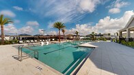 Located at 2507 Koji St in Mount Dora, Florida, this single-story community pool facility offers a well-appointed outdoor retreat designed for relaxation and recreation. The centerpiece is a generously sized swimming pool with crystal-clear water, featuring a gradual sun shelf entry and dedicated lounge areas along the pool deck. Tall, mature palm trees flank the pool, lending a tropical ambiance that complements the sunny Central Florida climate.

The pool deck is finished with light-toned pavers and is furnished with rows of lounge chairs, many shaded by navy blue market umbrellas and open-air cabanas, providing ample options for both sun-soaking and shaded relaxation. The surrounding landscape is thoughtfully designed with tropical plantings, ornamental shrubs, and decorative gravel beds that create a clean, resort-like aesthetic.

A covered pavilion anchors one side of the facility, featuring large windows, recessed lighting, an oversized ceiling fan, and stone-accented columns — offering a comfortable sheltered gathering space. The area is enclosed by sleek black aluminum fencing, ensuring both safety and an unobstructed view of the surrounding neighborhood and open sky. The facility is governed by posted pool rules, with operating hours from dawn to dusk.