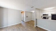 Located at 3210 Lynn Ridge Dr in Raleigh, NC, this single-floor home offers a well-organized layout with a clean, neutral aesthetic throughout. The open living area is a standout feature, showcasing warm wood-style flooring, soft gray walls, and a textured ceiling that adds character. A fireplace serves as a focal point in the living room, which also benefits from direct access to an outdoor area through a sliding glass door, allowing natural light to fill the space. The living and dining areas flow seamlessly, with a peninsula counter connecting to the kitchen. The kitchen is efficiently designed with white cabinetry, granite-style countertops, a double stainless steel sink, and black appliances including a range, refrigerator, and dishwasher. A dedicated laundry area provides the convenience of an in-unit washer and dryer. The hallway connects the main living spaces to additional rooms and a full bathroom featuring a tiled tub-shower combination. Throughout the home, consistent flooring, clean white trim, and a neutral color palette create a cohesive and move-in-ready environment suited for comfortable everyday living.