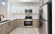 Located at 18412 Homestead Ave, Unit 218, in Miami, FL, this well-designed one-bedroom, one-bathroom residence offers a thoughtfully laid-out floor plan that maximizes every square foot of its compact footprint. The interior presents a cohesive modern aesthetic, with light wood-style luxury vinyl flooring and crisp white walls flowing throughout the space.

The kitchen is a standout feature, showcasing a two-tone cabinetry scheme that pairs white upper cabinets with warm wood-finish lower cabinets, accented by matte black hardware. A white quartz countertop extends to form a peninsula with a built-in sink, creating a functional breakfast bar and pass-through. Stainless steel appliances — including a refrigerator, electric range, and over-the-range microwave — complete the polished look. A subway tile backsplash and a pendant light fixture add refined detail.

The bedroom is a calm, bright retreat with a large window fitted with a roller shade, allowing for natural light control and privacy. Clean white walls and the same light flooring continue into this space, creating a serene atmosphere.

The bathroom features neutral large-format tile in the shower/tub surround and on the floor, complemented by a white vanity with black hardware, offering a spa-like feel. The overall ambiance of the unit is modern, clean, and move-in ready.