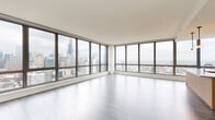 Located in Chicago's vibrant West Loop neighborhood, this high-rise residence at 164 N Peoria offers a sleek, contemporary design with an open, airy layout. The living area is defined by expansive floor-to-ceiling windows that wrap around the space, flooding the interior with natural light and framing sweeping panoramic views of the Chicago skyline, including the iconic Willis Tower. Light-toned hardwood flooring flows throughout, complementing the clean, neutral color palette.

The chef's kitchen is thoughtfully appointed with warm wood cabinetry, stone countertops, a striking stone tile backsplash, and premium stainless steel Bosch appliances, including a gas range and built-in wine cooler. A large island provides additional workspace and casual seating.

The bathrooms are finished to a high standard, featuring floating wood vanities with dual under-mount sinks, quartz countertops, large framed mirrors, and tiled glass-enclosed showers. A dedicated laundry room with a stacked Whirlpool washer and dryer adds everyday convenience.

A clean, well-lit hallway connects the private quarters, maintaining a sense of flow throughout the residence. Recessed lighting and a neutral, white-toned interior enhance the modern ambiance, making this an exceptionally refined urban living space.