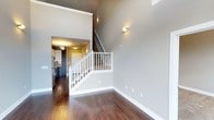 Located at 131 E Davie St in the vibrant heart of downtown Raleigh, North Carolina, this two-floor residence offers a thoughtfully designed living environment with a strong sense of openness and modern refinement. The main living area immediately impresses with dramatically high ceilings that amplify the sense of space, creating an airy and expansive atmosphere. Rich, dark hardwood flooring runs throughout, providing a warm contrast to the cool grey tones of the walls and the crisp white trim and baseboards. Wall-mounted sconce lighting adds a refined, architectural touch to the interiors. A white-railed staircase serves as a central design element, connecting the two floors in an elegant yet functional way. The kitchen, visible from the main living area, features dark cabinetry and stainless steel appliances, offering a sleek and contemporary look. An entry corridor with a door provides a clear sense of entry and separation between spaces. The two-floor layout allows for a natural distinction between living and private areas, making the space both practical and well-organized. Overall, the residence combines modern urban aesthetics with warm, inviting materials, making it a compelling offering in one of Raleigh's most sought-after downtown locations.