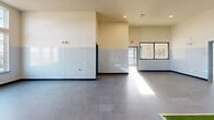 Located at 3700 Limestone Parkway in Gainesville, Georgia, this single-floor commercial facility is purpose-designed for pet care operations. The layout is thoughtfully organized to support efficient animal handling, offering a seamless flow from the entrance through each functional zone.

The entrance greets visitors with an interior glazed partition wall featuring large framed windows, providing a clear line of sight into the main activity area while maintaining separation between spaces. The main rooms are generously proportioned with notably high ceilings that enhance the sense of openness and airflow. Walls throughout are finished with a durable two-tone treatment — smooth white above and a wipe-clean panel wainscoting below — designed for easy sanitation. Speckled epoxy flooring in the activity areas adds both durability and a clean, professional appearance.

A dedicated kennel corridor features a row of stainless steel animal enclosures along one wall, concrete flooring with a central floor drain for easy cleaning, and a dark-painted ceiling that provides a calm, defined environment. A built-in artificial grass relief station is installed in the main activity area, further reflecting the facility's animal-focused design.

The laundry room is equipped with a full-size washer and dryer, supporting day-to-day operational needs. Consistent teal-painted doors and blue accent baseboards unify the interior aesthetic throughout. Recessed lighting and natural light from exterior windows keep the space bright and welcoming.