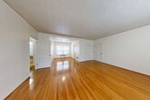 Located at 1640 NE Irving St in Portland, Oregon, this two-bedroom, one-bathroom residence offers a well-organized single-floor layout with a clean, functional design throughout. The expansive living room is a standout feature, showcasing polished hardwood floors that reflect natural light streaming through multiple windows fitted with classic blinds. A textured ceiling and baseboard heating units add character to the bright, neutral-toned interior.

The open living area flows naturally into the rest of the home, connecting through a hallway to both bedrooms and shared spaces. The primary bedroom is generously proportioned, continuing the warm hardwood flooring and featuring a window that brings in natural light. The second bedroom mirrors this aesthetic with its own window and the same gleaming floors, offering a comfortable and well-lit space.

The kitchen is galley-style, appointed with white cabinetry extending to the ceiling for ample storage, laminate countertops, a single-basin sink, and white appliances including a range and refrigerator. Tile flooring and a window above the counter keep the space practical and bright.

The bathroom includes a full tub-shower combination with tile surround, a window for natural ventilation, and baseboard heating. A connecting hallway ties all rooms together, providing an efficient and accessible flow throughout this well-maintained Portland residence.