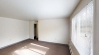 This single-floor unit offers a straightforward, functional layout across several well-defined rooms. The living area is generously sized, featuring neutral-toned carpet, crisp white walls, and multiple windows fitted with horizontal blinds that allow ample natural light to filter in. Baseboard heating runs along the walls, providing efficient warmth throughout. A ceiling fan with an integrated light fixture adds both comfort and practicality to the space.

The bedrooms continue the same carpeted flooring and neutral palette, each benefiting from natural light via sizable windows. At least one bedroom includes a closet with a hanging rod, offering convenient built-in storage.

The kitchen is compact yet well-organized, featuring white cabinetry above and below a laminate countertop with warm wood toning. A stainless steel sink, white refrigerator, and range are included, with vinyl flooring underfoot and abundant cabinet storage for everyday needs.

The bathroom presents a clean, utilitarian design with a pedestal-style sink, a wall-mounted medicine cabinet mirror, and a full soaking tub with a shower rod. A frosted privacy window above the tub provides natural light while maintaining seclusion. The overall ambiance of the unit is clean, bright, and move-in ready.