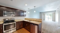 This single-floor residence offers a thoughtfully designed layout that balances functionality and comfort throughout. The kitchen serves as a standout feature, showcasing rich dark-espresso cabinetry, granite countertops, and a full suite of stainless steel appliances including a refrigerator, range, microwave, and dishwasher. Wood-look flooring runs through the kitchen, while pendant lighting above the peninsula adds a modern touch. The kitchen opens toward the living area, creating a connected, sociable flow. The living room is generously proportioned, carpeted in neutral tones, and filled with natural light through a large sliding glass door that provides direct access to an outdoor patio and views of surrounding greenery. The bedroom is equally well-sized, featuring plush carpeting, a window with outdoor views, and access to a spacious walk-in closet outfitted with multi-tiered wire shelving for efficient organization. The bathroom continues the design language of the kitchen, with dark cabinetry, granite countertops, a large vanity mirror, and wood-look flooring. Neutral wall tones and clean white trim throughout create a cohesive, calm aesthetic that makes the space feel bright, open, and move-in ready.