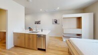 Located at 319 N Pottstown Pike in Exton, PA, this thoughtfully designed single-floor studio unit maximizes every square foot through smart layout planning and modern finishes. The space is accessed through a dedicated entrance featuring a solid dark-paneled door, opening into a bright, open-plan interior finished with light hardwood flooring and crisp white walls throughout.

The kitchen is a standout element, featuring warm wood cabinetry, stainless steel appliances including a refrigerator, range, microwave, and dishwasher, all anchored by a white quartz countertop peninsula with bar-height seating for two. Recessed lighting and a ceiling-mounted HVAC unit keep the space comfortable and well-lit.

A built-in bunk bed and shelving system is seamlessly integrated into one wall, offering efficient sleeping and storage solutions without compromising the open feel of the room. Natural light filters in through a window overlooking the surrounding area.

The unit includes two bathrooms, one of which features a sliding glass-door walk-in shower with large-format tile and a combined washer/dryer unit neatly tucked into a dedicated niche with overhead cabinetry. The overall design aesthetic is clean and minimalist, making this a highly functional and well-appointed space.