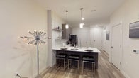 The Edge on 4th presents a thoughtfully designed single-floor residence that seamlessly blends contemporary style with everyday functionality. The open-concept kitchen serves as the heart of the space, featuring dark wood-grain cabinetry, a full suite of stainless steel appliances including a range, microwave, dishwasher, and French door refrigerator, and a white quartz countertop island with bar seating for four. Pendant lighting and white subway tile backsplash add modern character, while wood-look flooring runs throughout the main living areas, creating a warm and cohesive aesthetic. The bedroom is a well-appointed retreat, offering plush carpet, a ceiling fan, and window treatments that provide privacy and light control. A generously sized walk-in closet with built-in shelving and hanging space connects directly to a full bathroom, which is outfitted with dark wood vanity cabinetry, a quartz countertop, a large framed mirror, and a tub-shower combination. Adding to the unit's convenience, a stacked washer and dryer is tucked neatly within the floor plan, offering in-unit laundry without sacrificing living space. Clean lines, neutral tones, and modern finishes throughout lend the space a polished, move-in-ready feel.