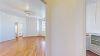 This well-organized 1-bedroom, 2-bathroom residence is thoughtfully laid out across a single floor, making efficient use of its cozy footprint. Warm, honey-toned hardwood floors run throughout, lending a cohesive and inviting character to every room.

The spacious primary bedroom stands out as the largest room in the unit, featuring two large multi-pane windows that usher in generous natural light and offer views of the surrounding neighborhood. A classic cast-iron radiator provides efficient heating, while a ceiling fan adds comfort year-round. The bedroom includes two closets, offering ample storage for its size.

The kitchen is clean and functional, outfitted in an all-white palette with paneled cabinetry, a full-size refrigerator, and simple countertops that maximize the available workspace.

The bathroom showcases classic subway tile work along the walls and surrounds a deep soaking tub with chrome fixtures — a timeless design detail that adds character to the space. A full-length mirror on the door enhances the sense of openness.

A hallway connects the rooms efficiently, and the overall layout flows naturally from one space to the next. The crisp white walls throughout the unit, combined with the warm flooring and abundant natural light, create a bright, clean, and comfortable living environment.