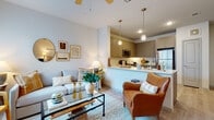 This single-floor residence offers a thoughtfully designed open-concept layout that seamlessly connects the living, dining, and kitchen areas. Light-toned luxury vinyl plank flooring runs throughout, lending a cohesive, clean aesthetic to the entire space.

The kitchen is a functional highlight, featuring sage-toned shaker-style cabinetry, stainless steel appliances including a refrigerator, range, and microwave, and a peninsula with pendant lighting overhead. A white countertop surface provides ample prep space, while a built-in dishwasher adds convenience.

The living area accommodates comfortable furnishings beneath a ceiling fan, with natural light filtering through window treatments. Adjacent to the living space, a defined dining area sits near an in-unit laundry closet housing a full-size washer and dryer, with additional utility storage above.

The primary bedroom benefits from large windows that invite natural light and features light-wood flooring, ample wall space, and access to a walk-in closet. A second bedroom offers similar finishes with a dedicated closet and space for a work area. The bathroom includes a tub-shower combination with tiled surround, a vanity with storage cabinetry, and matching wood-look flooring, completing the unit's consistent and polished interior design.