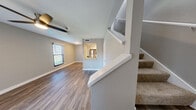 Located at 1111 Vista Valet in San Antonio, TX, this two-story, one-bedroom, one-bathroom residence offers a thoughtfully designed layout spread across two floors. The main level houses the combined kitchen and living area, featuring wood-style flooring, neutral gray walls, and ceiling fans that contribute to a clean, contemporary aesthetic. A sliding glass door with vertical blinds opens the living area to an outdoor view, allowing natural light to fill the space. The kitchen is well-appointed with white shaker-style cabinetry, granite countertops, stainless steel appliances including a range, dishwasher, refrigerator, and built-in microwave, all complemented by light wood-tone flooring. A carpeted staircase leads to the upper level, where the generously sized primary bedroom features plush carpet, dual windows that invite natural light, and a ceiling fan. The upper floor also includes access to a closet and the full bathroom, which showcases a white vanity with granite countertops, brushed nickel hardware, and a well-lit mirror above the sink. The overall design is cohesive and modern, with a neutral color palette and quality finishes throughout.