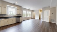 Located at 40 Jones St in Providence, Rhode Island, this single-floor residence offers a thoughtfully designed open-concept layout that seamlessly connects the kitchen and living areas. The kitchen is well-appointed with white shaker-style cabinetry, dark granite countertops, and a full suite of stainless steel appliances, including a refrigerator, range, over-the-range microwave, and dishwasher. Wide-plank wood-style flooring runs throughout the main living space, lending warmth and continuity to the interior. Multiple windows along the main living area invite an abundance of natural light while providing views of the surrounding greenery. Recessed lighting throughout enhances the clean, modern aesthetic. The bathroom features marble-look tile flooring, a sliding glass walk-in shower, and a white vanity, creating a bright and polished finish. The overall color palette of soft grays and crisp whites gives the space a fresh, contemporary feel. The efficient floor plan, as revealed by the dollhouse view, includes clearly defined areas for living, cooking, and bathing, making excellent use of the available space.