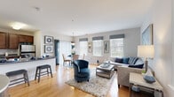 Located at 198 Camelot Ct in Cinnaminson, NJ, this well-appointed 2-bedroom, 2-bathroom single-floor residence offers a thoughtfully designed layout with a bright, open feel throughout. The entryway hallway, accented by large-scale artwork, leads directly into the open-concept living, dining, and kitchen area. The living room features warm hardwood flooring, multiple windows with natural light, and generous space for comfortable seating arrangements. The adjacent dining area flows seamlessly from the living room, complete with a pendant light fixture overhead. The kitchen is equipped with rich dark wood cabinetry, stainless steel appliances including a gas range, microwave, and refrigerator, paired with grey countertops and a tile floor. A breakfast bar provides additional seating and separation between the kitchen and living areas. Both bedrooms are carpeted and well-lit with large windows. The primary bedroom is notably spacious and includes a walk-in closet with wire shelving. The two bathrooms feature tile flooring, dark wood vanities, and a glass-enclosed shower. A dedicated in-unit laundry area houses a full-size washer and dryer with overhead shelving, adding everyday convenience to this comfortable, move-in-ready home.