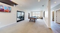 Located in Taylors, SC, this single-floor community amenity space offers a well-appointed game room and supporting facilities designed for comfortable, social use. The main game room is bright and open, anchored by a solid wood billiards table with a dark felt surface set atop plush, patterned carpet. Recessed lighting and a striking tray ceiling accent with LED lighting illuminate the room, while large windows along one wall invite ample natural light and views of the surrounding community. A comfortable lounge seating area near the windows provides a relaxed gathering spot. Framed artwork decorates the walls, lending a polished, contemporary aesthetic. Black-framed glass doors open to an adjacent fitness area, adding versatility to the space. An eco boutique kiosk with a refrigerated display and product shelving is conveniently situated near the stairway entrance, offering easy access to refreshments and essentials. A connecting hallway, finished with wood-look luxury vinyl flooring and sage-toned walls, leads to three well-maintained bathrooms. Each bathroom features wall-mounted pedestal sinks, framed mirrors, and ADA-compliant grab bars, reflecting thoughtful accessibility design. Safety fixtures including a fire extinguisher cabinet are also present throughout. The overall ambiance is clean, modern, and welcoming.