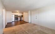 This single-floor unit is arranged in an open-concept layout that connects the living area directly to the kitchen, creating a cohesive and functional flow throughout the space. The living area is finished with neutral-toned carpet, providing a comfortable foundation, while textured ceilings run consistently throughout the unit.

The kitchen stands out as a well-appointed area, featuring stainless steel appliances including a refrigerator, electric range, and dishwasher. White shaker-style cabinetry lines the walls, complemented by granite-look countertops and a dark subway tile backsplash that adds a modern contrast. Wood-style hard flooring grounds the kitchen and entry areas.

Adjacent to the main living space, additional rooms offer carpeted or tile flooring and are illuminated by windows fitted with horizontal blinds, allowing natural light to filter in. Each room is equipped with baseboard heating, and at least one room also features a wall-mounted air conditioning unit, ensuring year-round climate control.

A closet with paneled doors provides convenient storage near the entry. The overall ambiance of the unit is clean, bright, and functional, with a neutral color palette that offers a versatile backdrop throughout.