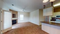 This single-story home offers a practical and comfortable layout with several well-defined living spaces. The living room serves as a central gathering area, featuring warm wall-to-wall carpeting, a ceiling fan, and a fireplace framed by a tiled surround with a built-in niche above the mantle, adding a distinctive focal point to the room. Adjacent to the living area, the kitchen is efficiently designed with cream-toned cabinetry, dark granite-style countertops, tile flooring, and white appliances including a range, microwave, and refrigerator. A breakfast bar peninsula connects the kitchen to the neighboring carpeted dining or flex space, providing additional functionality.

A separate room with abundant natural light, a ceiling fan, and direct access to an outdoor deck offers a versatile secondary living or sitting area. The bedrooms are carpeted and feature neutral walls, natural light from windows, and closets with bifold doors for ample storage. Two full bathrooms are each equipped with a tub-shower combination, tile flooring, and vanity storage. Throughout the home, neutral tones and consistent finishes create a cohesive and move-in-ready atmosphere.