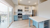Located at 13972 Edgewood Ave in Savage, MN, this thoughtfully designed one-bedroom, one-bathroom residence offers a clean, modern aesthetic throughout its efficiently utilized single floor. Light-toned luxury vinyl plank flooring runs through the main living areas, complemented by crisp white walls and recessed lighting that keep the space feeling bright and open.

The kitchen is a standout feature, boasting two-tone cabinetry with white upper cabinets and soft blue-gray lower cabinets, white quartz countertops, a classic subway tile backsplash, and a full suite of stainless steel appliances including a range, microwave, dishwasher, and refrigerator. A kitchen island provides additional prep and dining space. A large sliding glass door floods the area with natural light and opens to a private balcony with views of the surrounding neighborhood.

A hallway with a sliding barn door connects the living areas to the private quarters. The bedroom features plush carpeting, a spacious sliding-door closet, and a wall-mounted utility panel, offering both comfort and practicality. The bathroom is finished with white cabinetry, a single-sink vanity with light countertops, a full tub-shower combination, and matte black hardware accents that add a contemporary touch throughout.