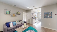 Located at 8204 Baltimore Ave in College Park, Maryland, this single-floor unit offers a well-designed layout with a contemporary aesthetic throughout. The open-concept living area features warm wood-look flooring, neutral walls, and lively décor accents, creating an inviting and functional space. A comfortable sitting area flows seamlessly into the kitchen and dining zone, making it ideal for both relaxing and entertaining.

The kitchen is outfitted with white cabinetry, dark countertops, and modern hardware, complemented by a dedicated dining nook with a round table and natural light streaming through a large window with views of the surrounding neighborhood.

The bedrooms are compact yet thoughtfully arranged, each featuring large windows that invite abundant natural light and views of the adjacent streetscape. Built-in shelving and practical storage solutions maximize the utility of each room.

Two full bathrooms serve the unit, each featuring a shower-tub combination, wood-look flooring, and clean white finishes. One bathroom includes a dark countertop vanity with white cabinetry and open wall shelving for added storage.

Overall, the unit presents a bright, modern living environment with cohesive design details, making it a practical and stylish option in the College Park area.