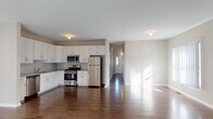 This two-story home offers a thoughtfully designed layout that balances open communal spaces with comfortable private quarters. The main level centers around an open-concept living and kitchen area, where rich, dark hardwood floors extend throughout. The kitchen is well-equipped with white shaker-style cabinetry, granite countertops, a subway tile backsplash, and a full suite of stainless steel appliances including a gas range, microwave, dishwasher, and refrigerator. The adjacent living area is generously sized, filled with natural light from multiple windows, and anchored by a fireplace, creating a warm and inviting atmosphere. A full bathroom on the main level features light tile flooring, a bathtub-shower combination, and a vanity with granite countertops. The upper level is accessed via a staircase and features a long hallway leading to the bedrooms, each finished with plush carpet and sliding closet doors. A dedicated bathroom on the upper level includes a glass-enclosed walk-in shower, a window for natural light, and light tile flooring. Throughout the home, clean white trim, neutral wall tones, and consistent hardwood flooring on the main level contribute to a cohesive, modern aesthetic.