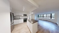 Located at 545-565 Belmont Ave W in Kitchener, Ontario, this well-appointed 2-bedroom, 1-bathroom unit offers a thoughtfully designed single-floor layout with a clean, modern aesthetic throughout. The open-concept kitchen and living area forms the heart of the home, featuring white shaker cabinetry, a subway tile backsplash, dark countertops, stainless steel appliances including a refrigerator, range, and over-the-range microwave, and a central island that provides additional workspace and storage. Light wood laminate flooring runs seamlessly throughout the unit, enhancing the bright and airy feel. The expansive living area is a standout feature, anchored by a sweeping curved bay window that wraps around the corner, flooding the space with natural light and offering pleasant views of the surrounding neighbourhood and mature trees. Both bedrooms are well-sized, with the primary bedroom offering generous proportions, a sliding closet, and a window framing outdoor greenery. The second bedroom also benefits from a window with natural light and a closet. The bathroom is elegantly finished with subway tile surrounding the bathtub and shower, stone-look floor tiles, a white vanity with an undermount sink, and chrome fixtures throughout. The overall ambiance is fresh, clean, and move-in ready.