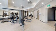 Located at 1425 Block Line Rd in Kitchener, Ontario, this well-appointed fitness centre offers a thoughtfully designed single-floor layout encompassing a generously sized training environment. The space is accessed through a dedicated entrance that leads into the main gym area, finished with light-toned luxury vinyl flooring and a clean, neutral colour palette throughout.

The primary workout area is bright and open, illuminated by a grid of recessed pot lights and a suspended tray ceiling that adds architectural definition. Large windows along the perimeter invite natural light and provide exterior views, enhancing the sense of space. The room accommodates a comprehensive range of strength and cardio equipment, including cable machines, adjustable benches, dumbbells, and weight racks, all arranged to allow comfortable circulation. Full-length mirrors line one wall, visually expanding the space and supporting proper form during training.

A secondary room, finished in a deep charcoal grey, serves as a functional and flexibility training zone. It features a medicine ball rack and ample open floor space for stretching or bodyweight exercises, with a window offering natural light. A decorative partition with a striking diagonal-stripe pattern marks the transition between zones, adding a contemporary design accent. The overall ambiance is modern, clean, and professional, suited to a wide range of fitness activities.